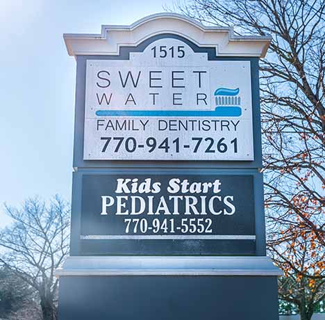 Outdoor sign for Sweet Water Family Dentistry with phone number 770-941-7261 and Kids Start Pediatrics with phone number 770-941-5552 under a clear blue sky.