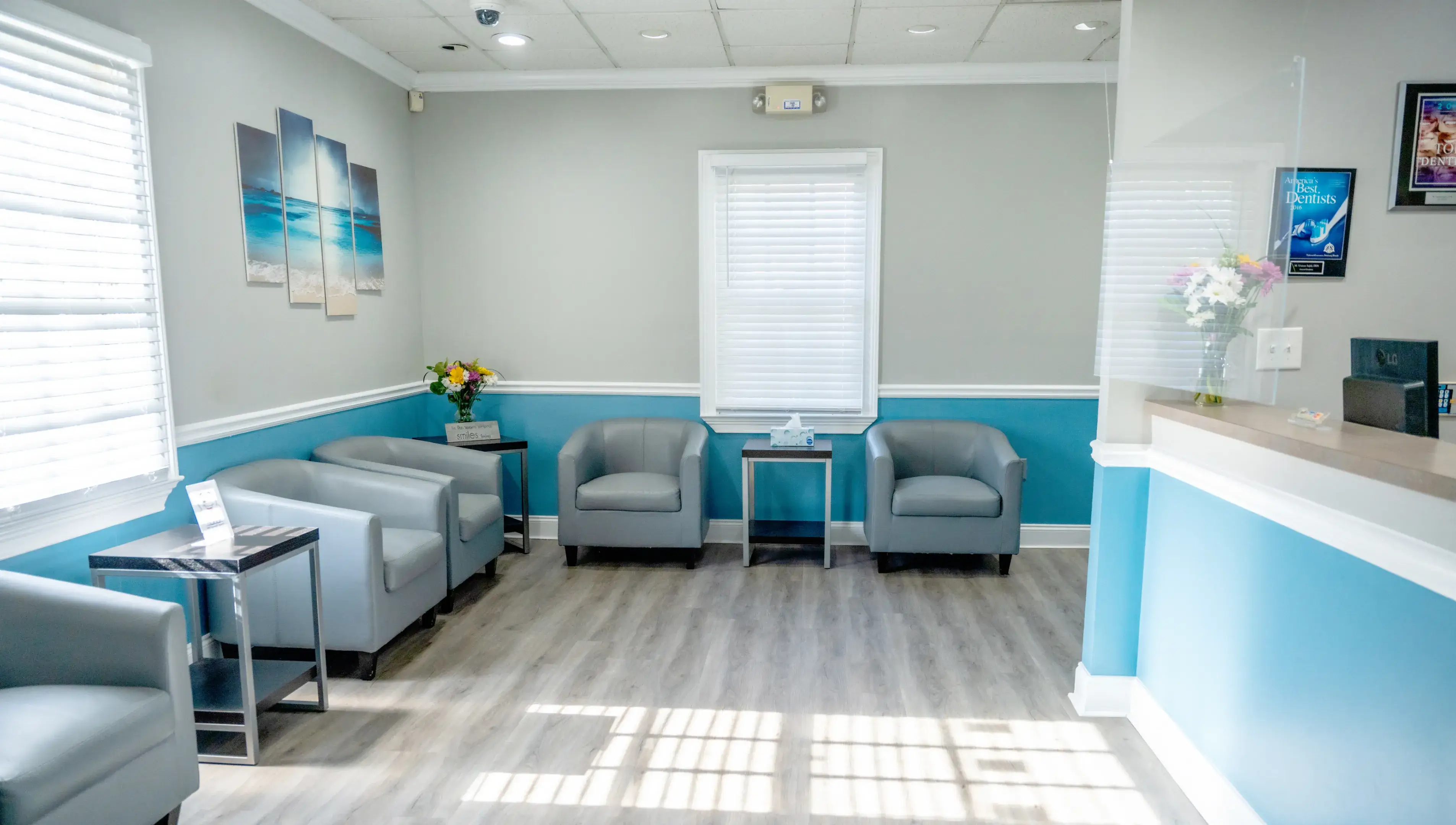 Bright waiting room with gray armchairs, blue and gray walls, wood flooring, and floral decorations.