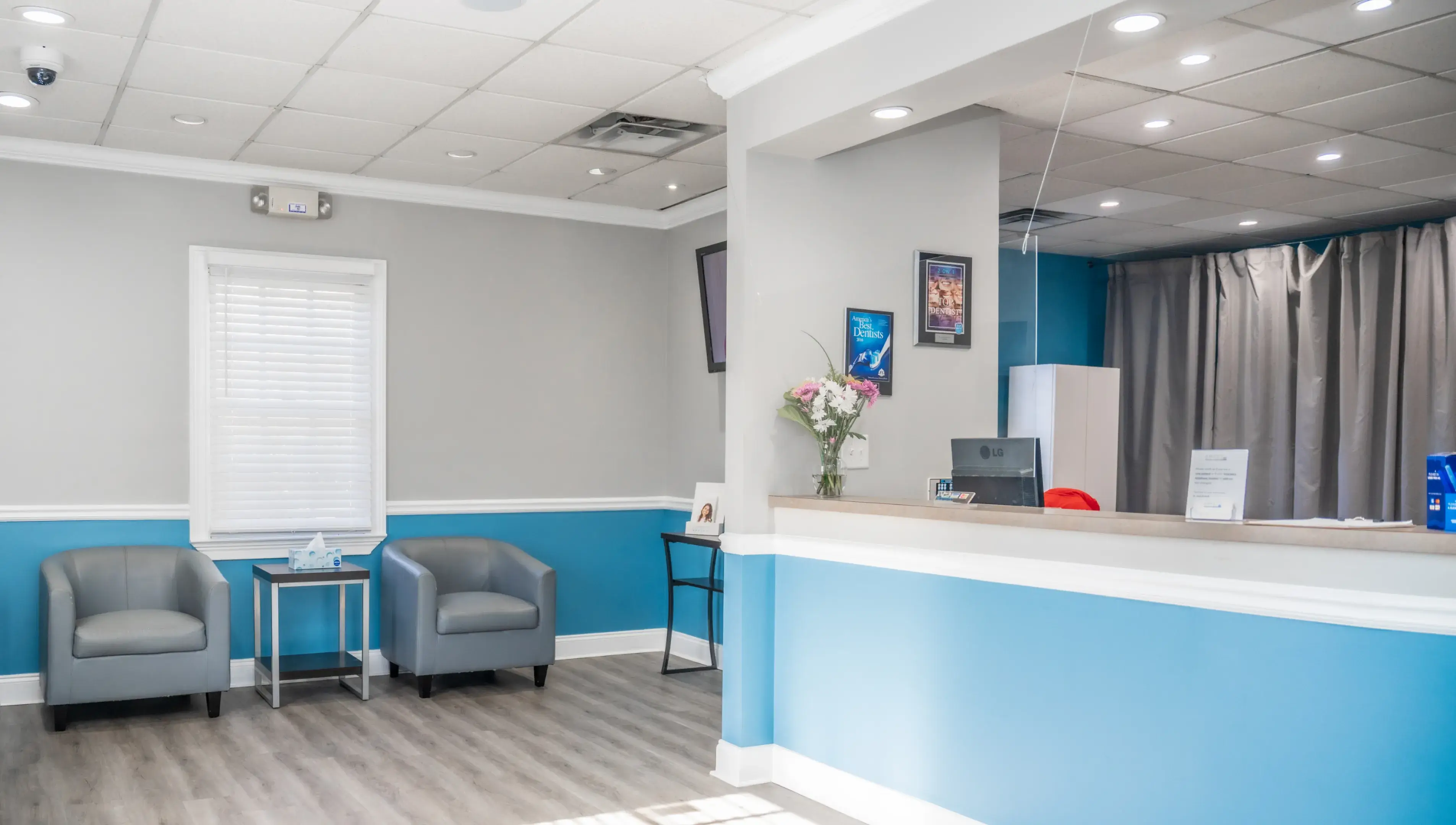 Bright waiting area with two gray armchairs, a small table with tissues, and a reception desk with a flower vase.